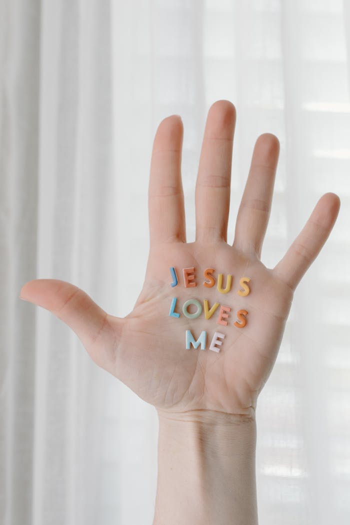 Offerings An open hand with colorful letters reading Jesus Loves Me against a soft curtain backdrop.